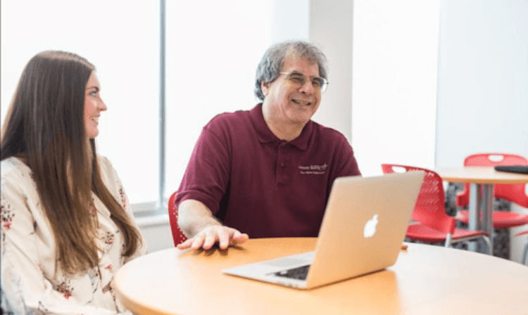 Professor carl scheraga laughs with student at desk in dsb.
