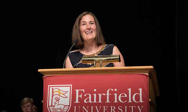 A person stands behind a podium that reads “Fairfield University”.