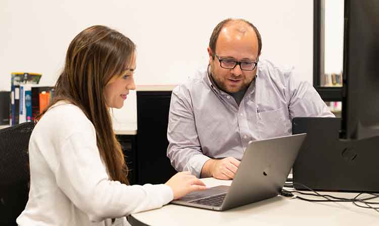 Image of a man and woman collaborating on a laptop in a modern office setting, focused on their work.