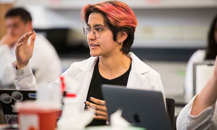 A student in a white lab coat speaks in class.