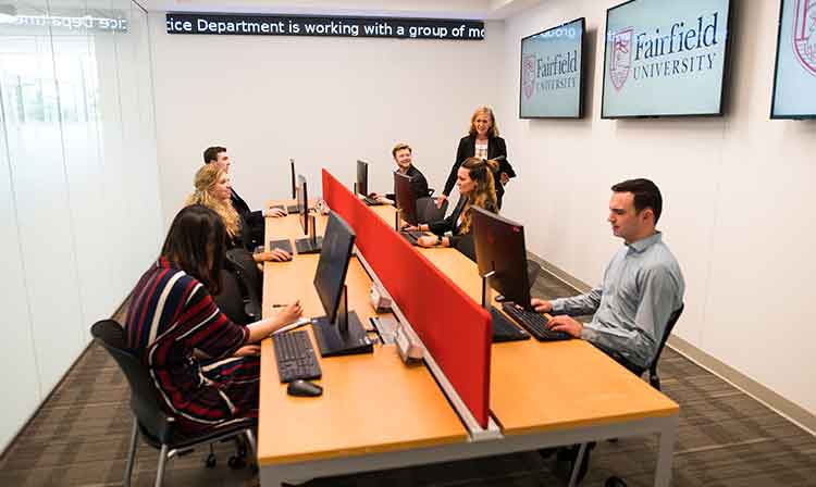 A class works in a lab with news and stock ticker on wall