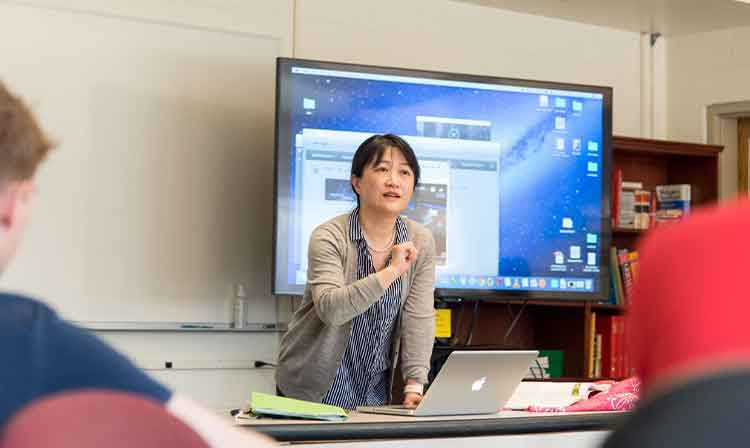 Asian Studies professor teaching a class in front of a large screen. 