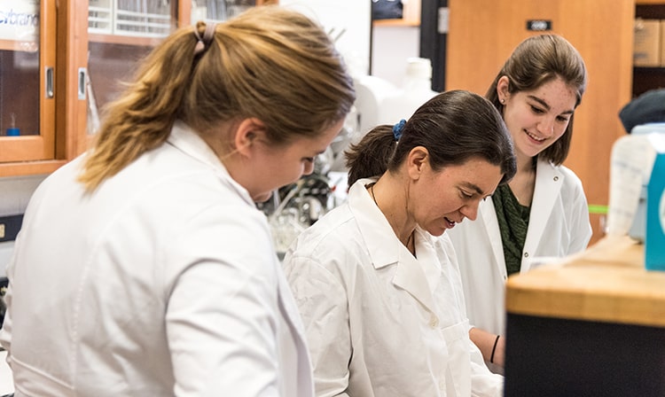 Students participating in a lab where the professor demonstrates pipetting techniques offscreen.