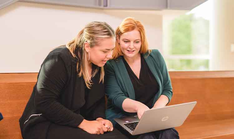 A professor helps a student with work on a laptop.