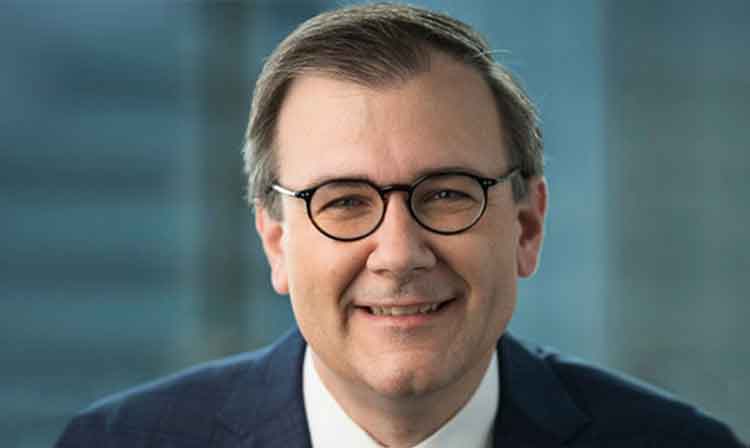 A man in glasses and a suit smiling confidently at the camera.