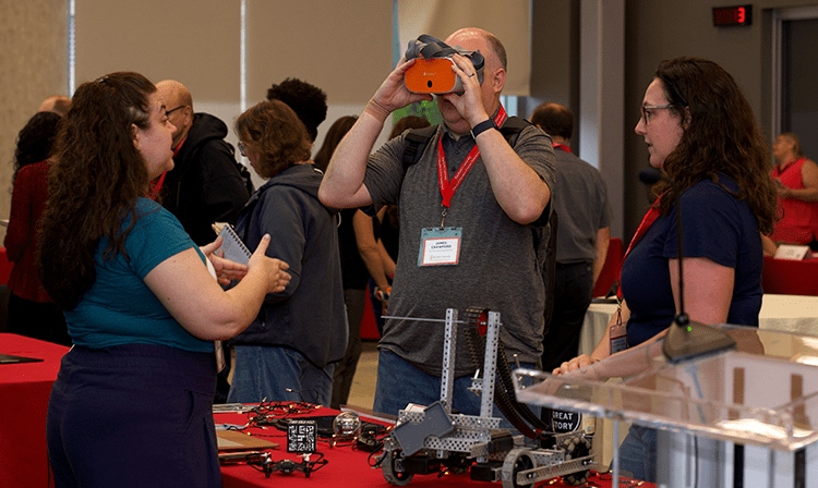 Forum participants interacting with technology (smart goggles) at a student's tech demo table.