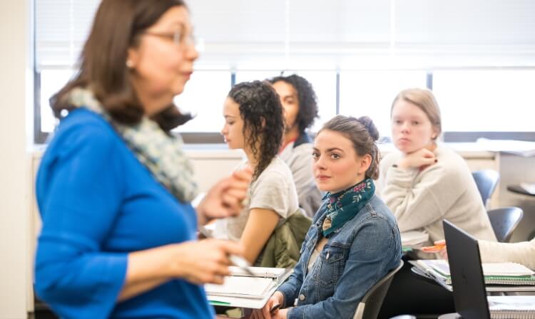 A professor addresses a class while four students watch.