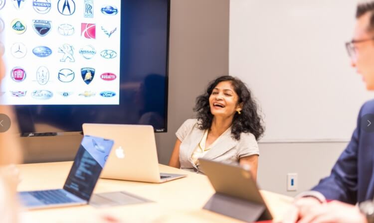 Student laughs with image of car brands on screen behind her. 