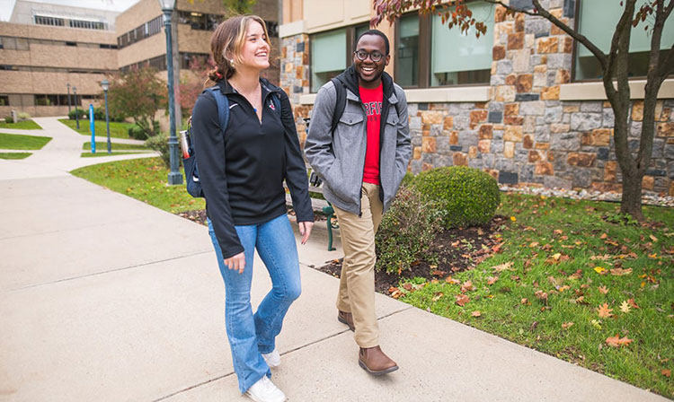 Two students smiling and walking through campus on a sunny day. 