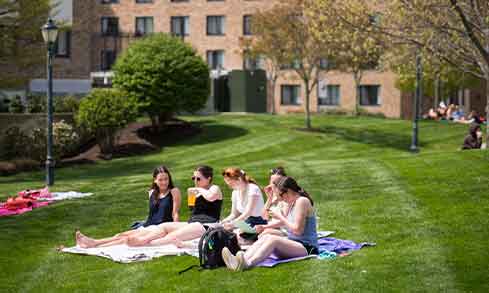 Students sit on a blanket as they enjoy a sunny day on the campus quad.