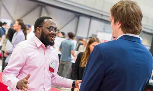 Two men engaged in conversation at a job fair, exchanging ideas and networking opportunities in a professional setting.