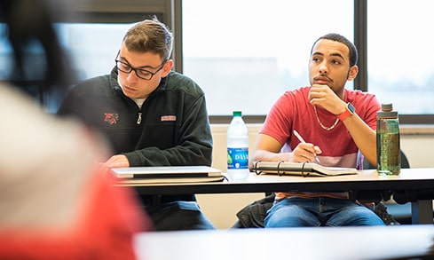 Two students listening intently during a lecture while one of them takes notes.