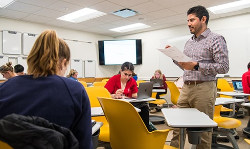 A professor talks to students while holding a piece of paper in a classroom. 