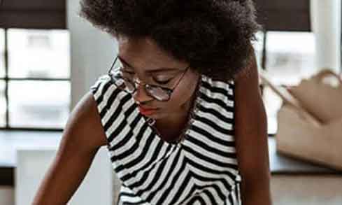 A woman i a black and white striped shirt is drawing at a desk.