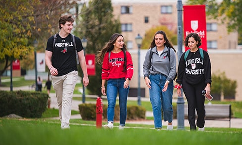 Four students walk outdoors in front of a Fairfield University banner.