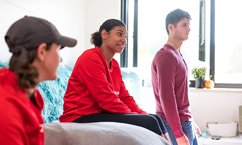 Three students stand in a dorm room.