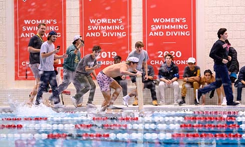 A student uses an engineered machine to attempt to walk on water in a swimming pool while other students watch.