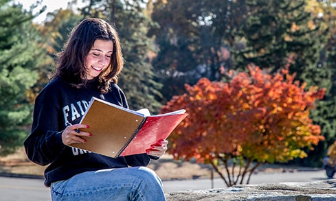 Student sitting outside and reading through the week's plans — written in a spiral notebook.