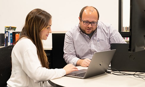 Student and professor sitting and working collaboratively on a laptop.