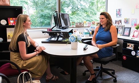 Two people sit at a round table in an office.