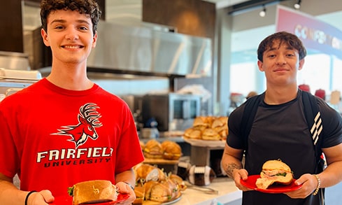 Three students in chef hats and aprons cooking during an on-campus dining event.
