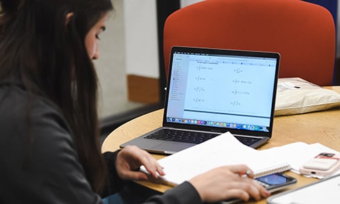 A student reads through their notes in front of an open laptop screen.