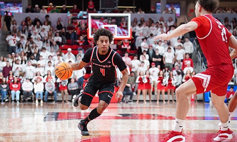 Men's basketball player in a red jersey dribbling the ball towards the net.