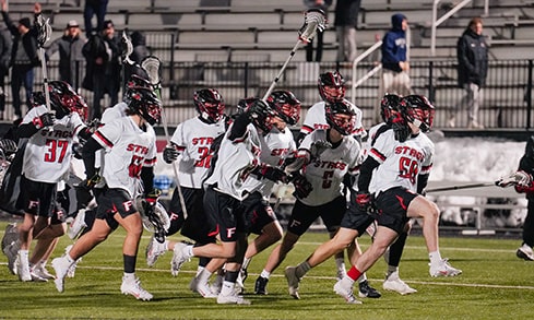 Men's lacrosse team yelling and charging onto the field, eager to begin their game.