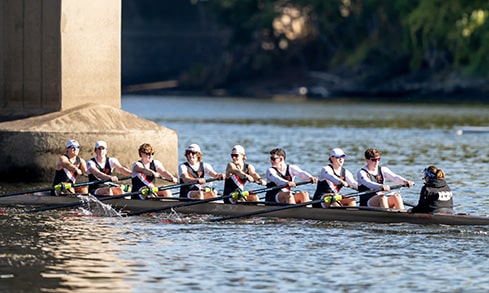 A crew boat of eight with the coach at the helm glides along the water during practice.