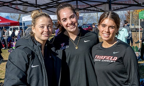 Female student-athlete cross country members posing together at a campus sports fair.