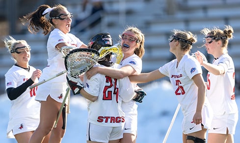 Female student-athletes celebrating a goal during their lacrosse game.
