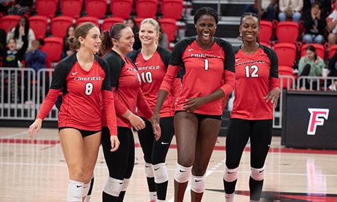 Five volleyball female student-athletes walking together onto the court to start their match.