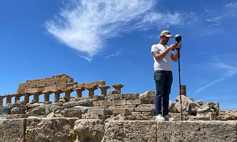 Ancient Mediterranean Studies team surveyor setting up a camera in the ruins of old architecture on a bright, sunny day.