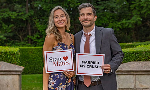 A Fairfield University alumni couple, referred to as 'StagMates', holding both a namesake sign and a sign that reads, 'Married my crush!'.