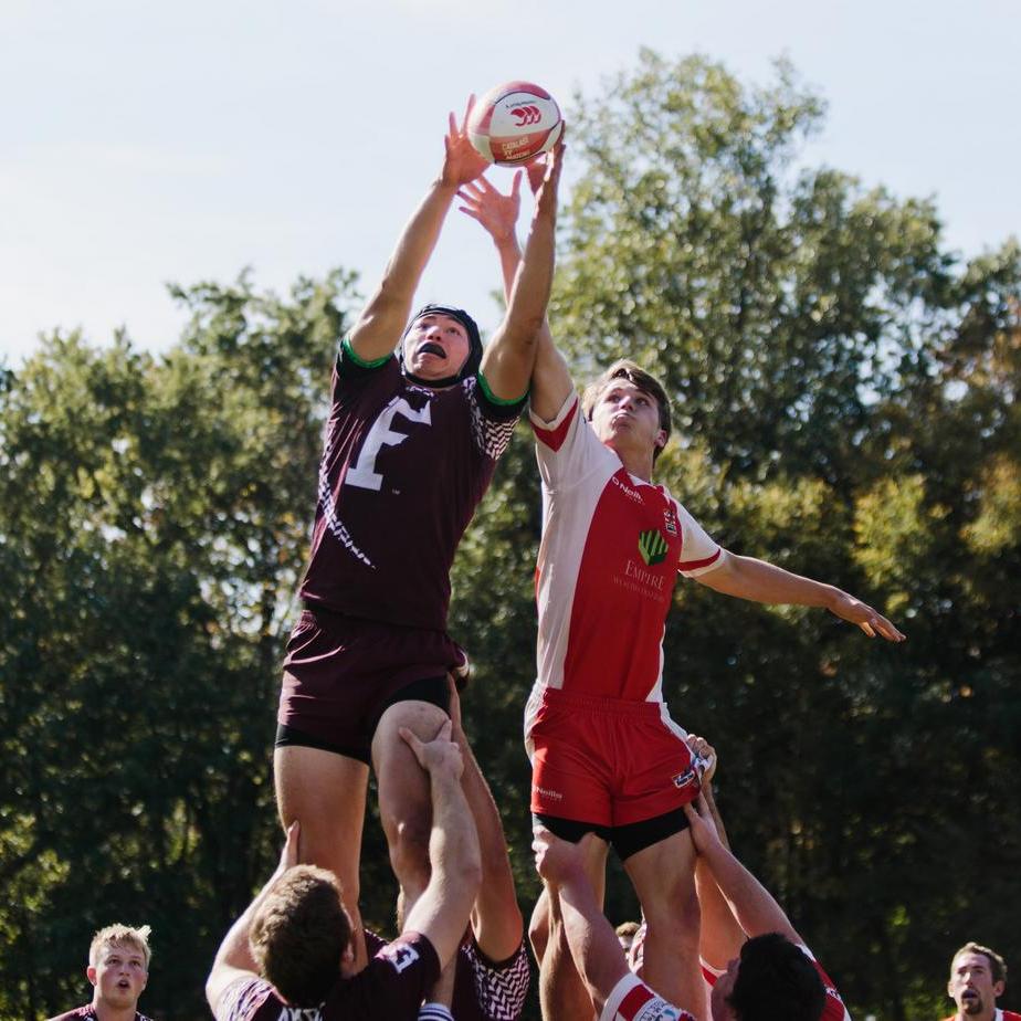 Two rugby players are lifted to reach the rugby ball outdoors.