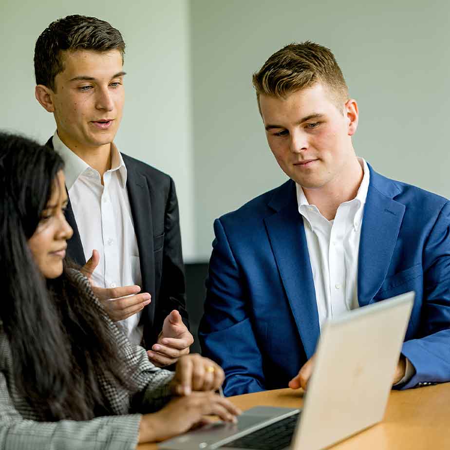 Three professionals in business attire collaborate while examining a laptop screen together.