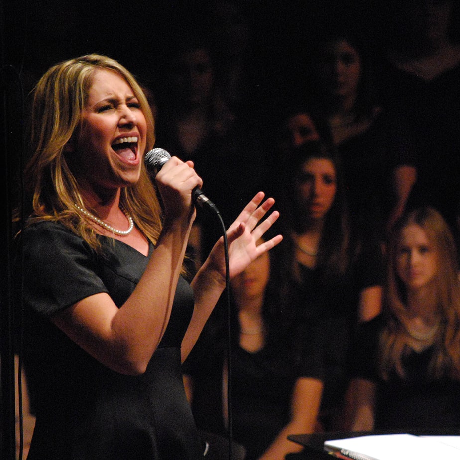 A student sings into a microphone in front of a crowd of people.