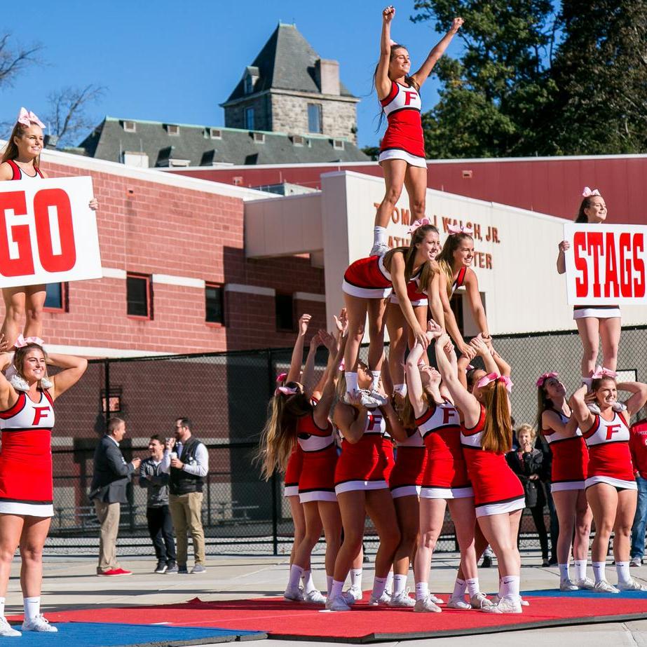 Cheerleaders make a pyramid while two others hold signs saying "Go Stags" 