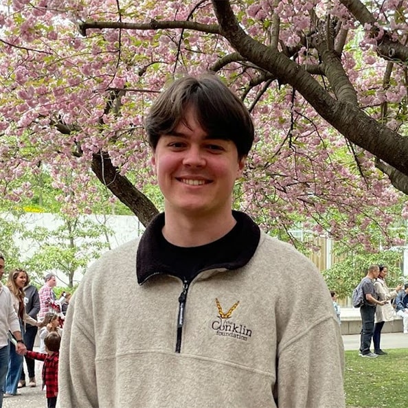 Dean Hartl smiles outdoors in front of a cherry blossom tree.
