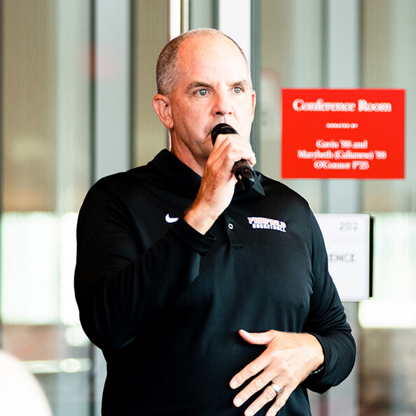 A man addressing an audience while speaking into a microphone.  
