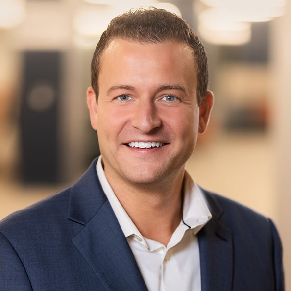 Young male Executive DBA candidate dressed in a blue suit smiling and posing against a white background.