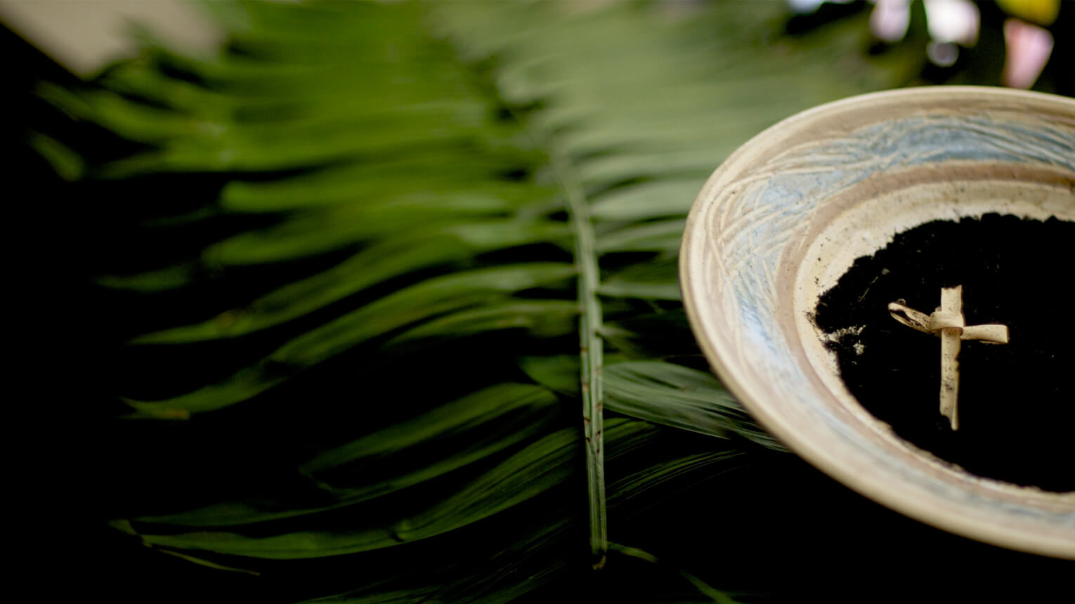 A bowl filled with dirt topped by a wooden cross, symbolizing Spirituality. 