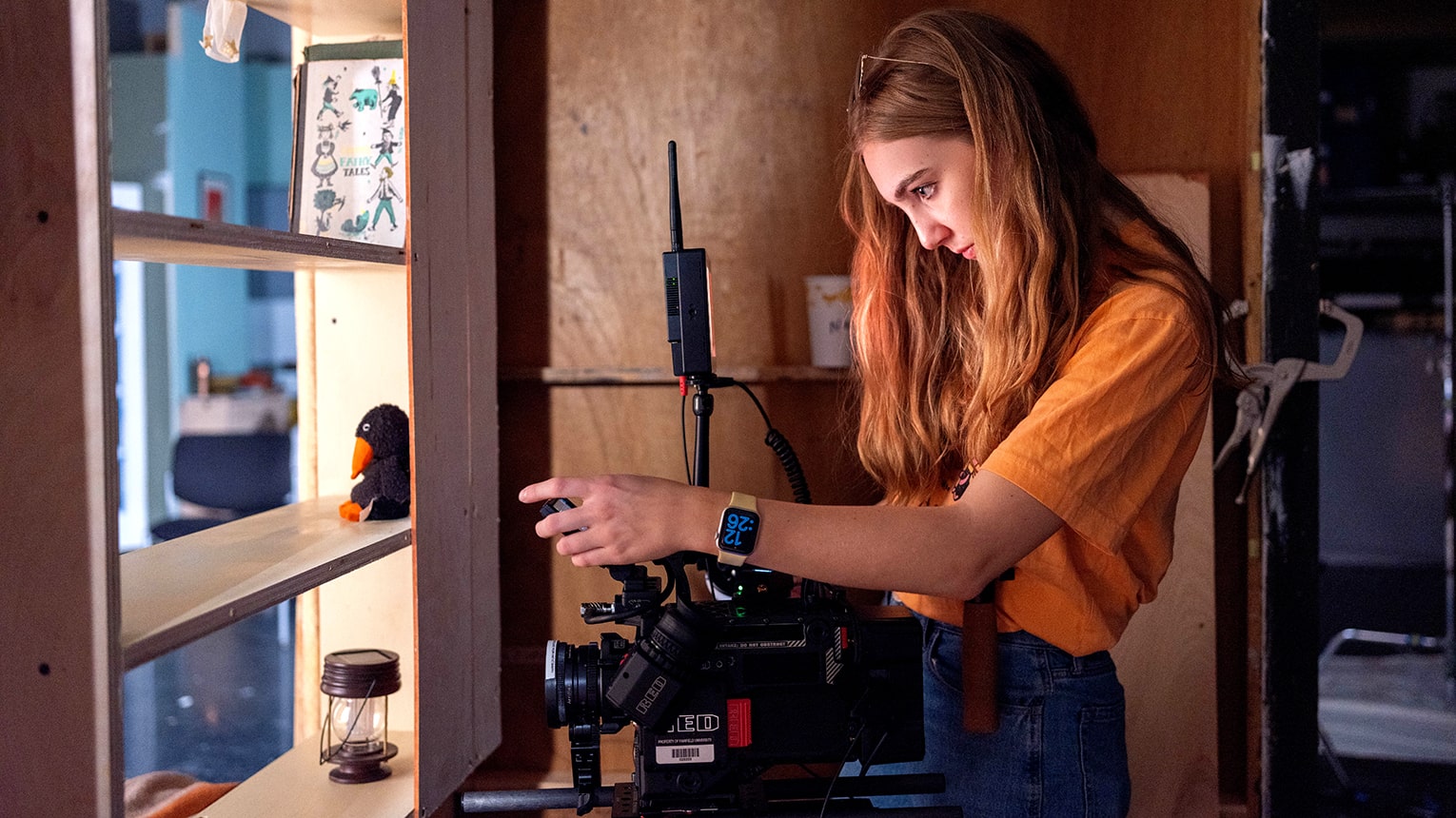 Female student adjusting a film camera lens as she sets up a shot behind a glass cabinet.