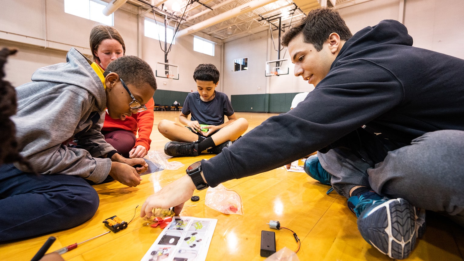 Fairfield engineering student working with elementary school kids on building battery-powered toy cars.