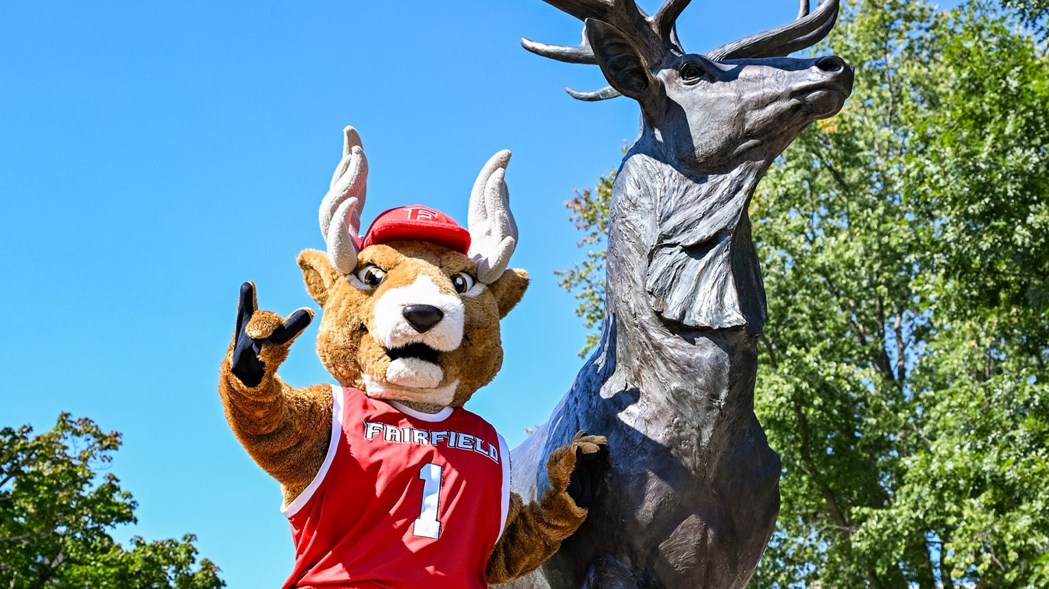 Lucas the Stag (mascot) posing with the 'Stags Up' hand sign next to the Lucas the Stag statue.
