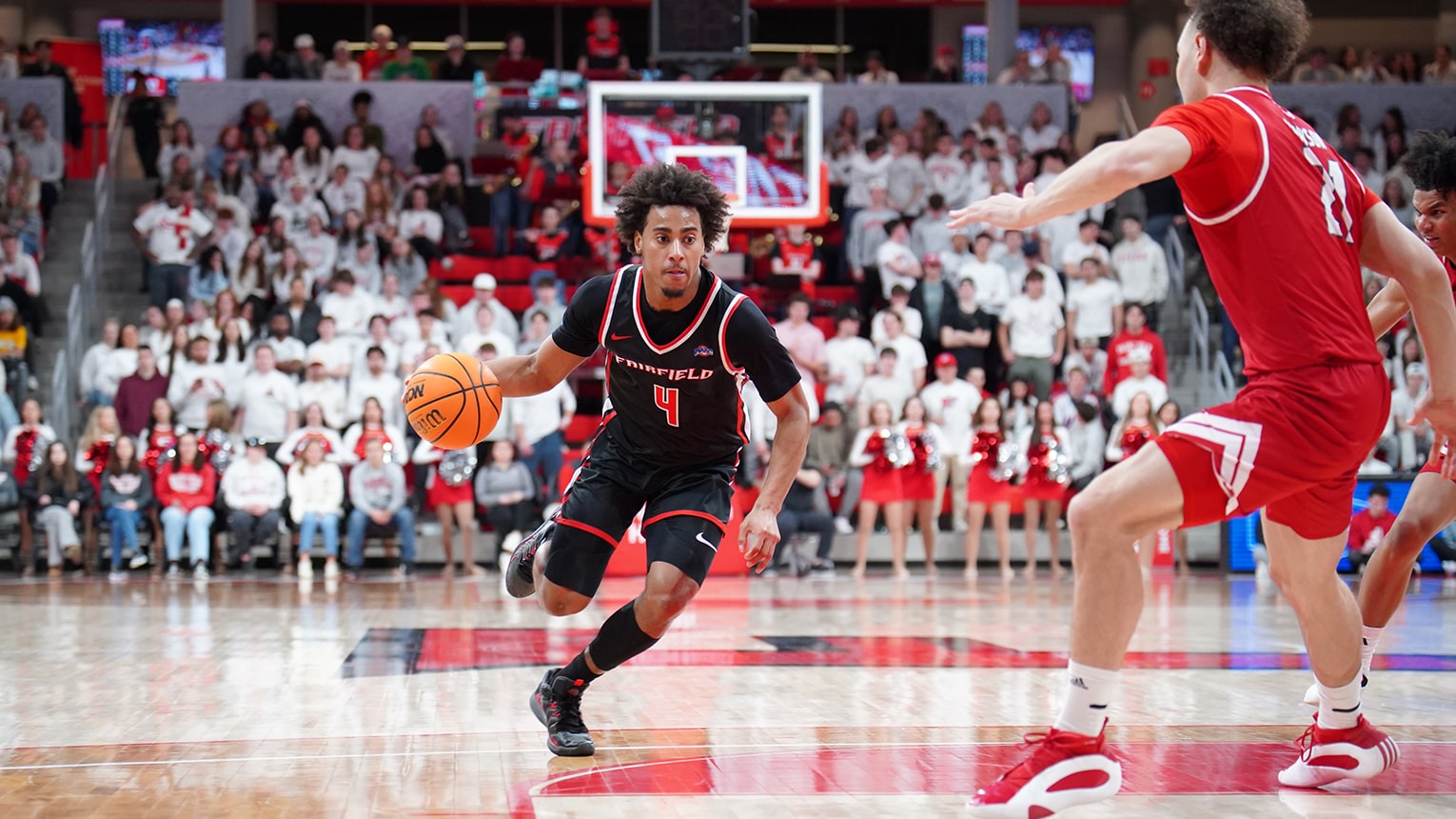 Men's basketball player in a red jersey dribbling the ball towards the net.