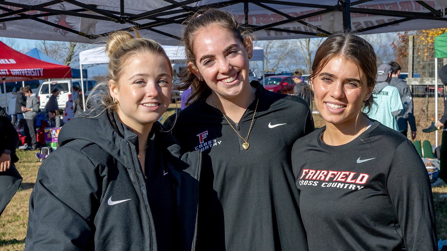 Female student-athlete cross country members posing together at a campus sports fair.