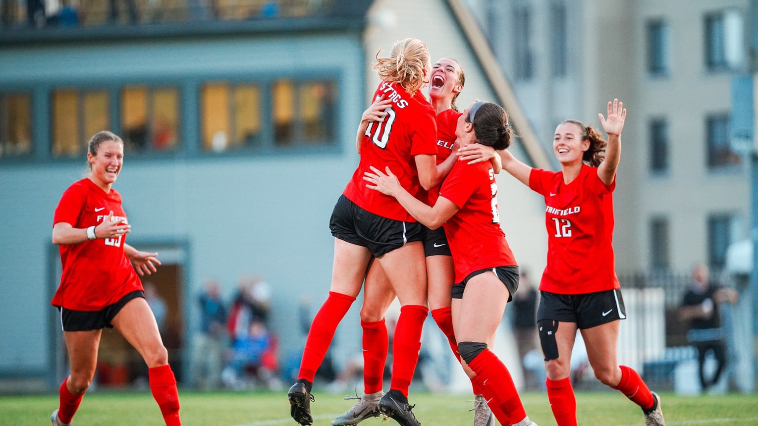 Women's soccer players jumping with joy together after scoring a goal.