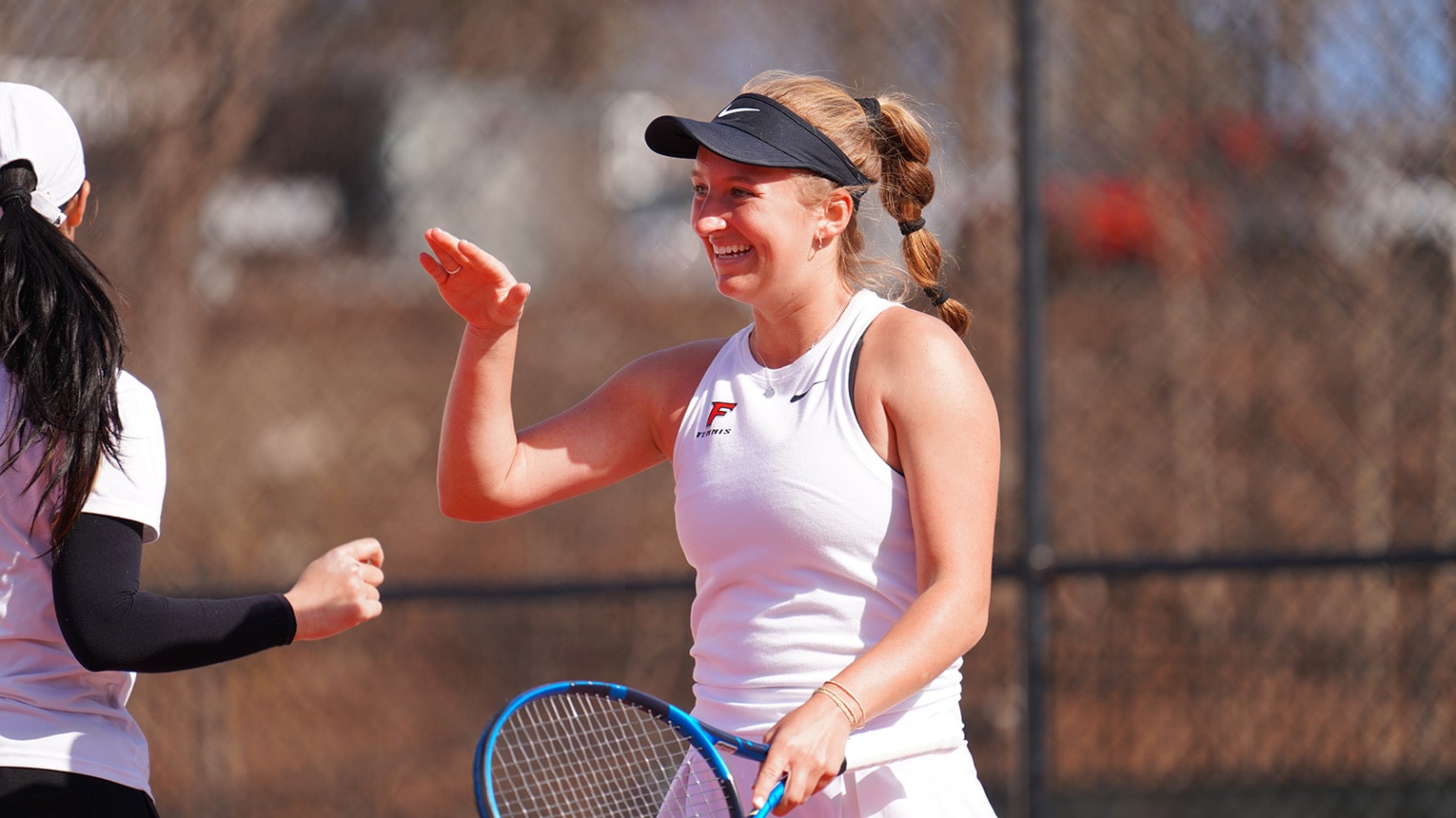 Female student-athlete high-fiving her teammate during tennis practice.