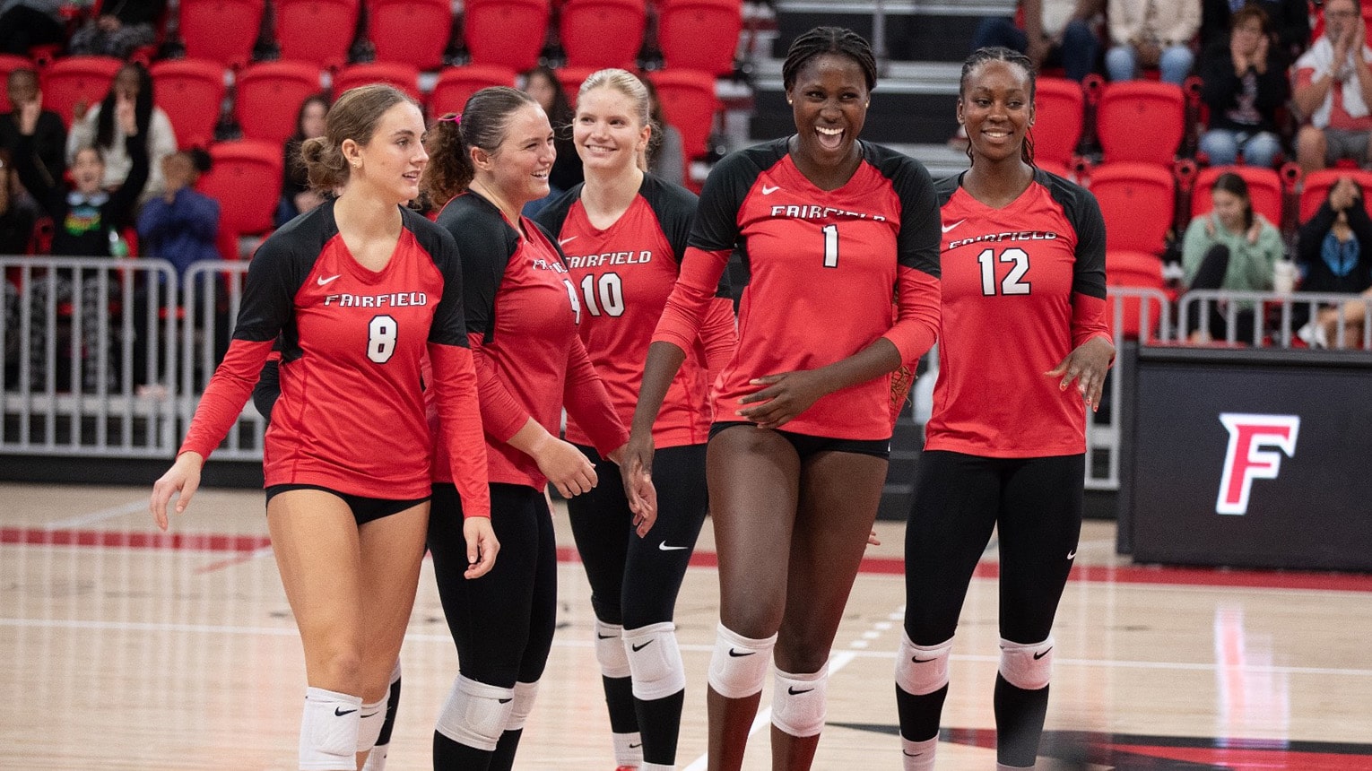 Five volleyball female student-athletes walking together onto the court to start their match.